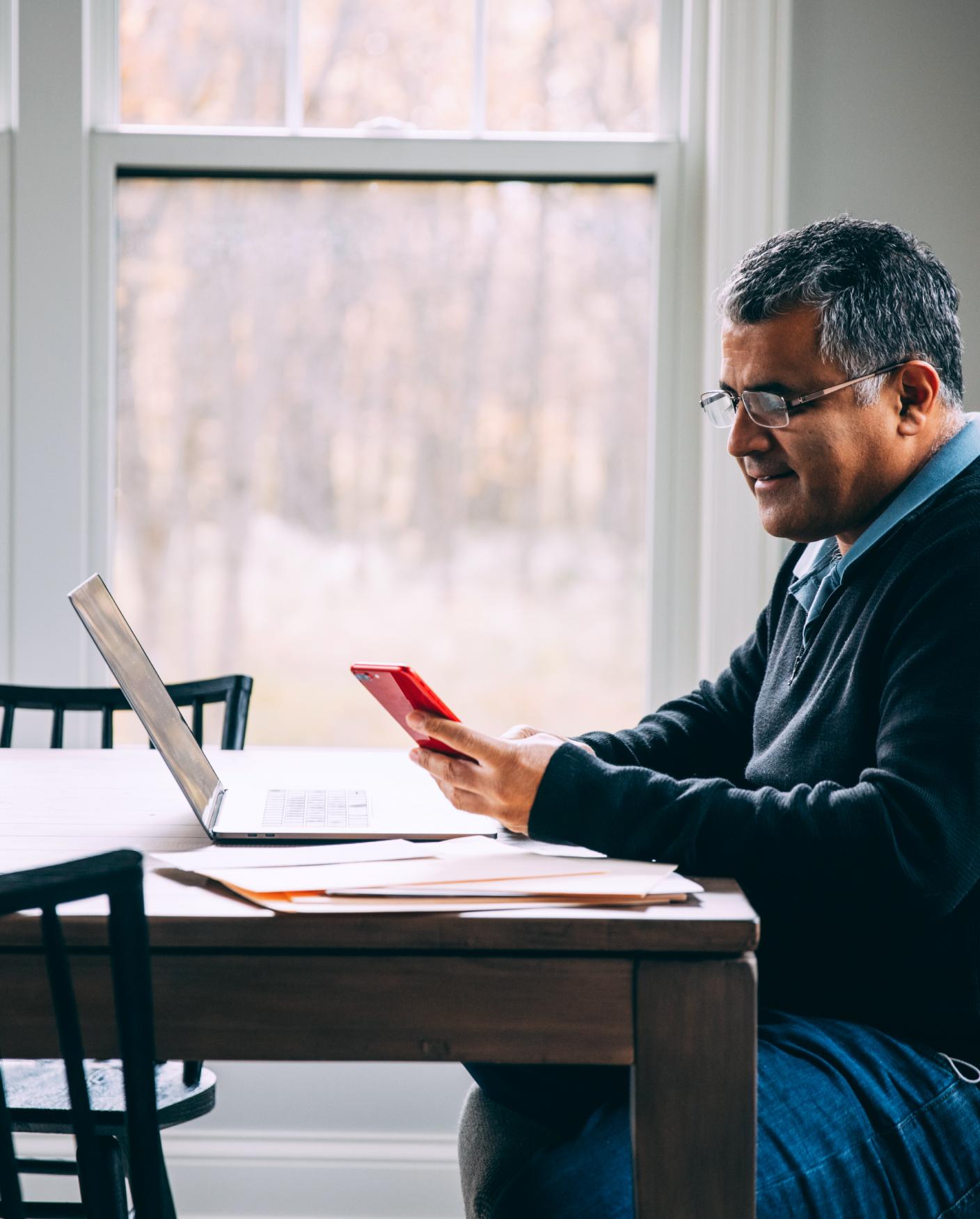 Man sits at kitchen table with laptop and phone